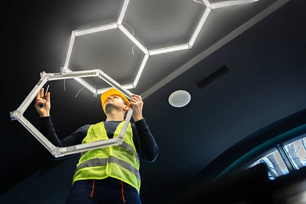 Installer fitting a geometric LED light fixture to a dark ceiling